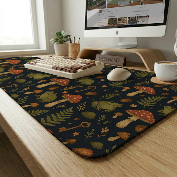 Dark forest-themed desk mat with an all-over pattern of frogs, mushrooms, fern leaves, acorns, tiny flowers, and antique keys.