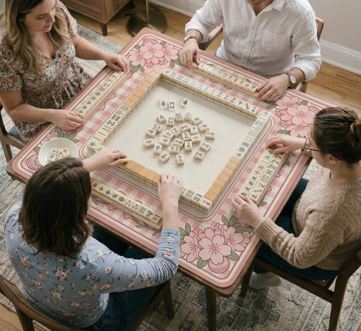 Square pink mahjong mat with a gingham border, floral corner details, and ribbon accents on a light background.