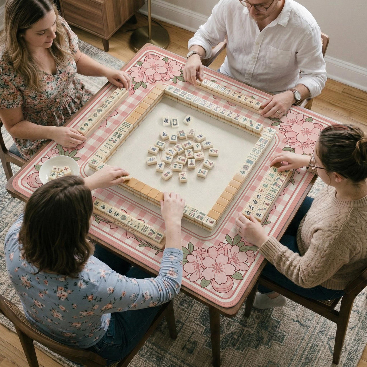 Square pink mahjong mat with a gingham border, floral corner details, and ribbon accents on a light background.