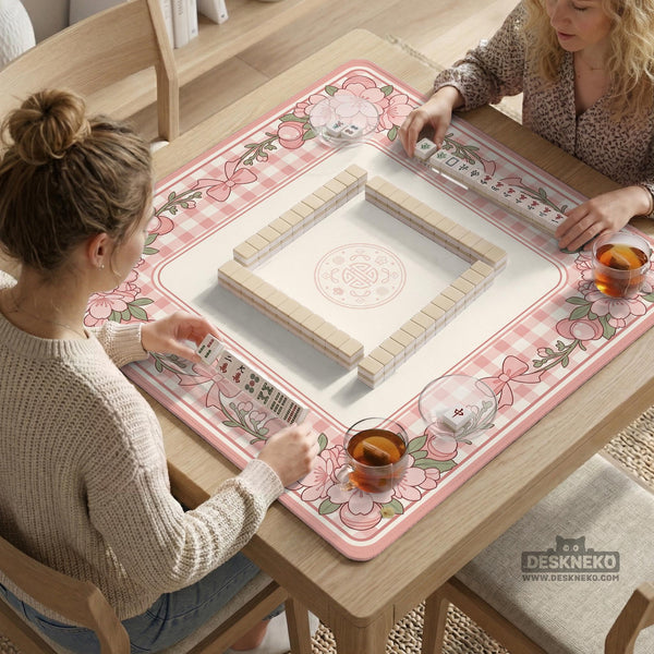Square pink mahjong mat with a gingham border, floral corner details, and ribbon accents on a light background.