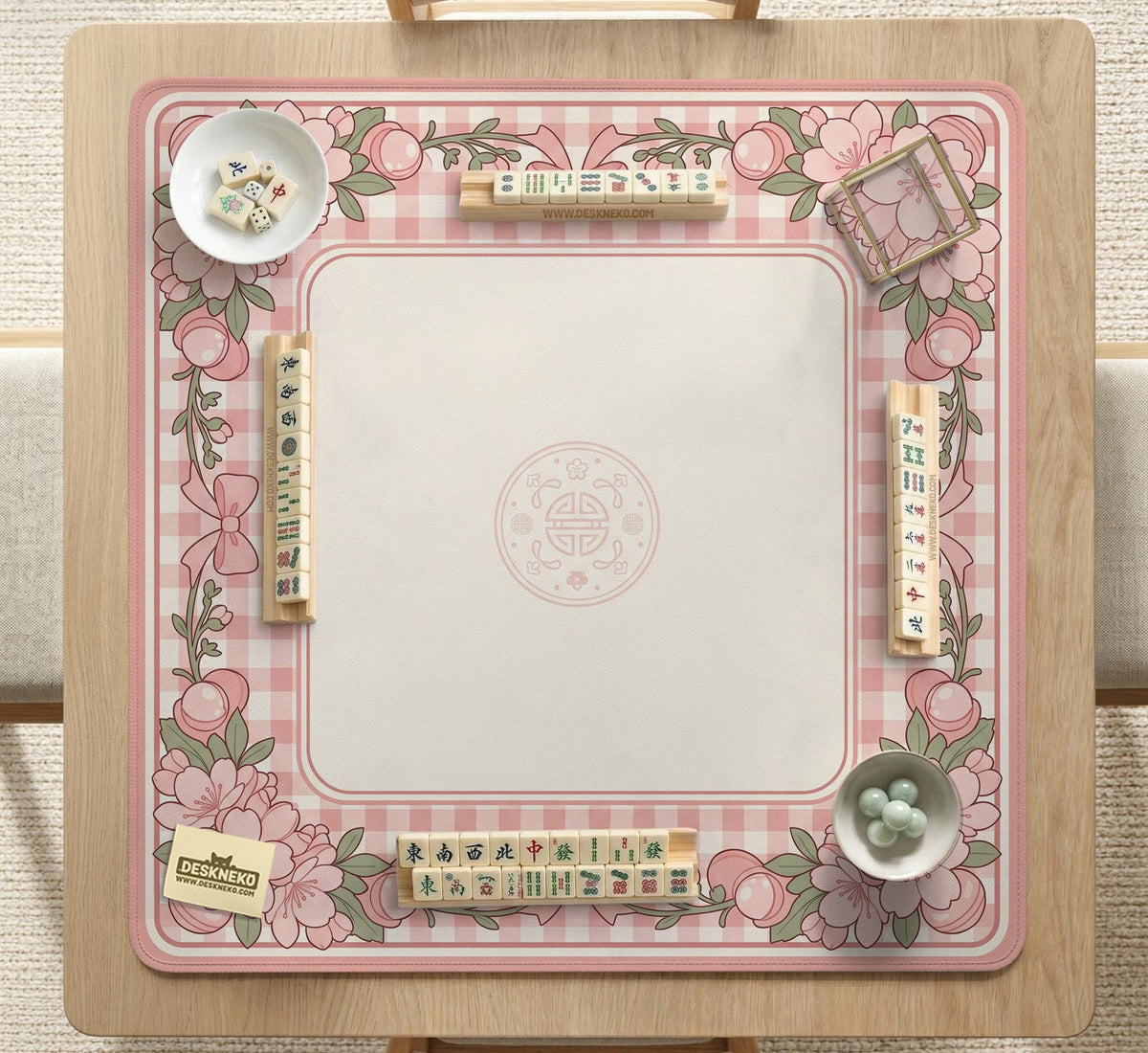 Square pink mahjong mat with a gingham border, floral corner details, and ribbon accents on a light background.
