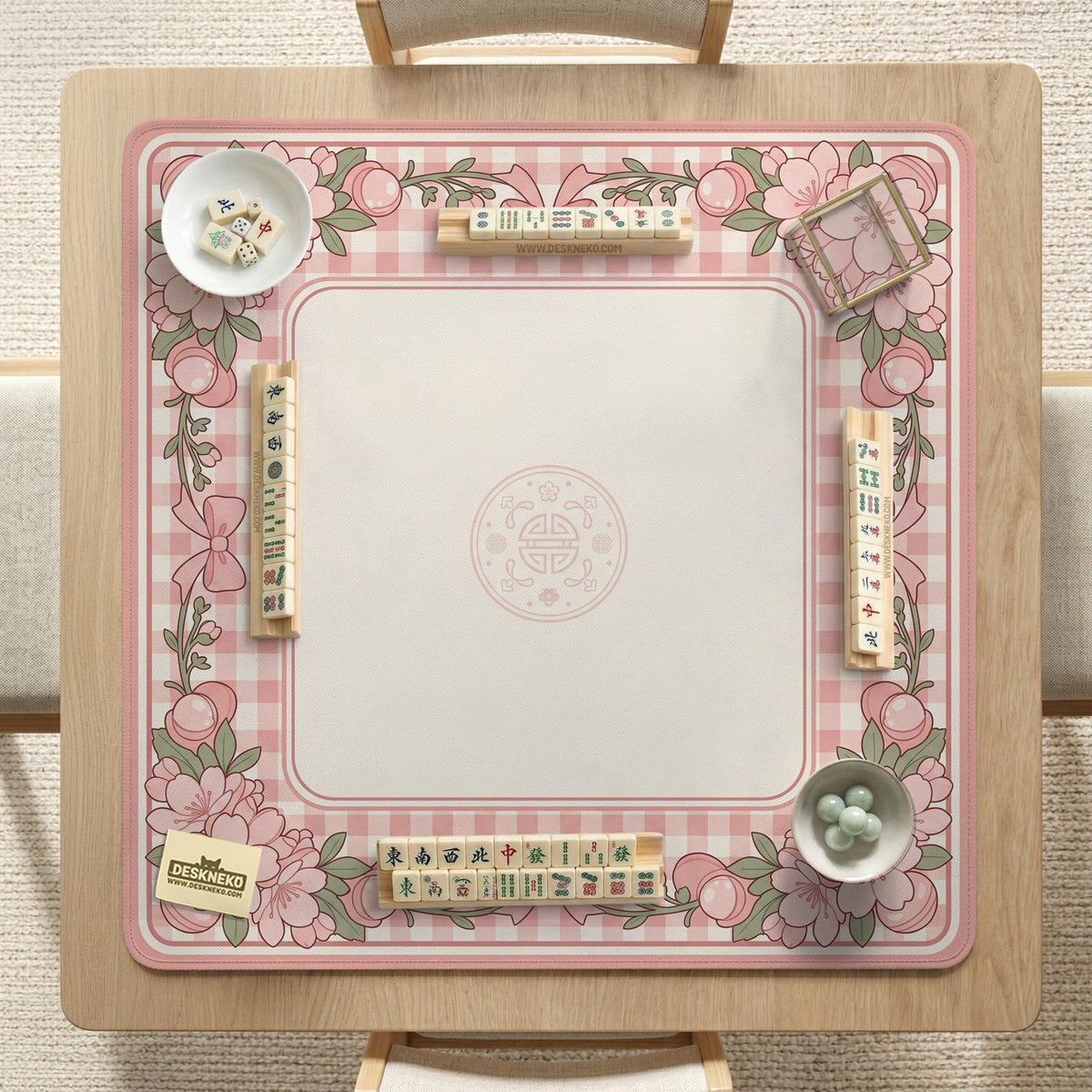 Square pink mahjong mat with a gingham border, floral corner details, and ribbon accents on a light background.