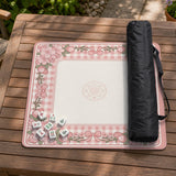 Square pink mahjong mat with a gingham border, floral corner details, and ribbon accents on a light background.