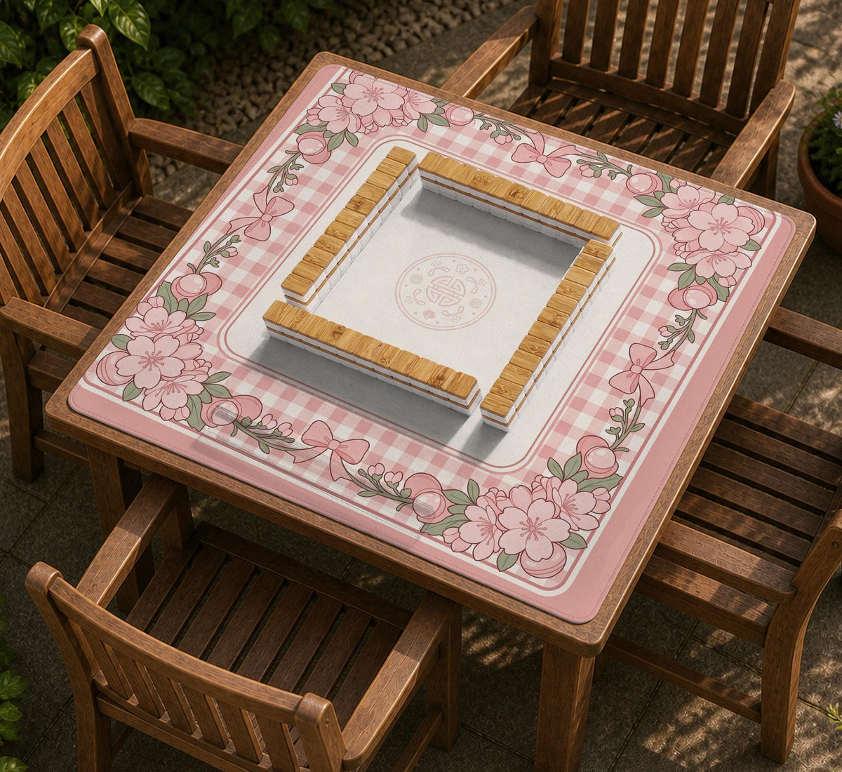 Square pink mahjong mat with a gingham border, floral corner details, and ribbon accents on a light background.