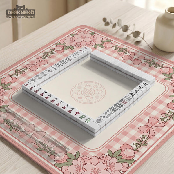 Pink gingham mahjong mat with a floral border, cherry blossom details, and a bow design around a plain center play area.