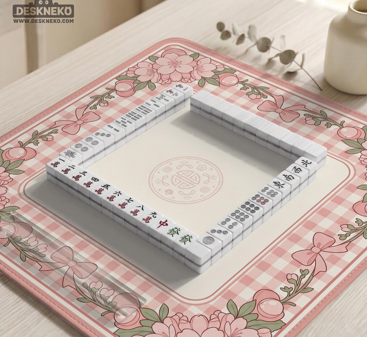 Square pink mahjong mat with a gingham border, floral corner details, and ribbon accents on a light background.