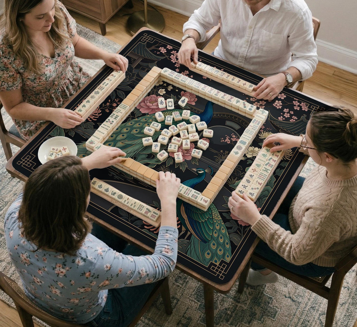 Square black mahjong mat with a gold peacock, blush flowers, and dark botanical artwork on a dark background.