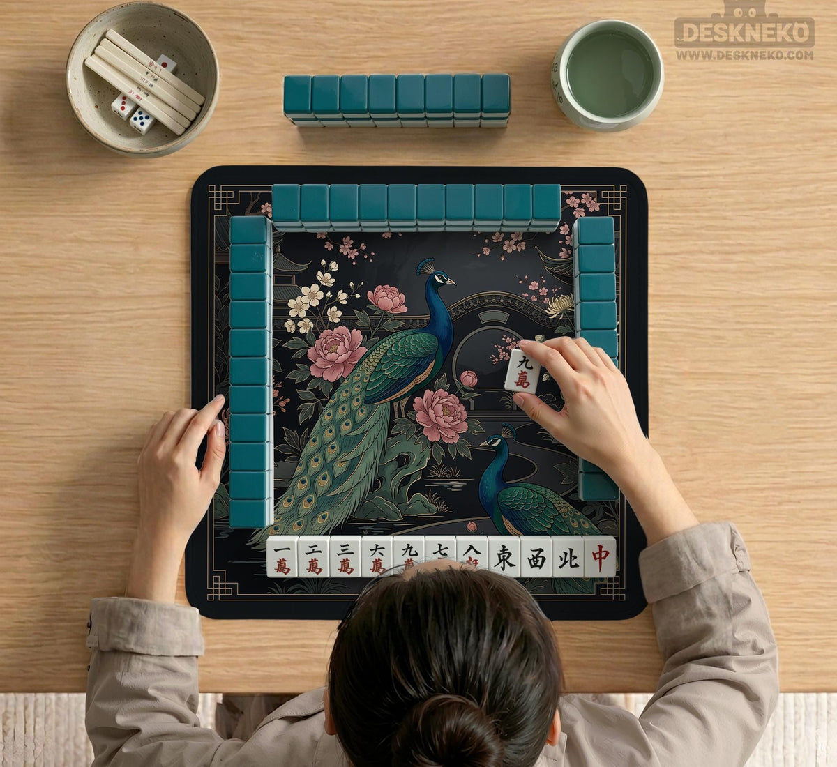 Square black mahjong mat with a gold peacock, blush flowers, and dark botanical artwork on a dark background.