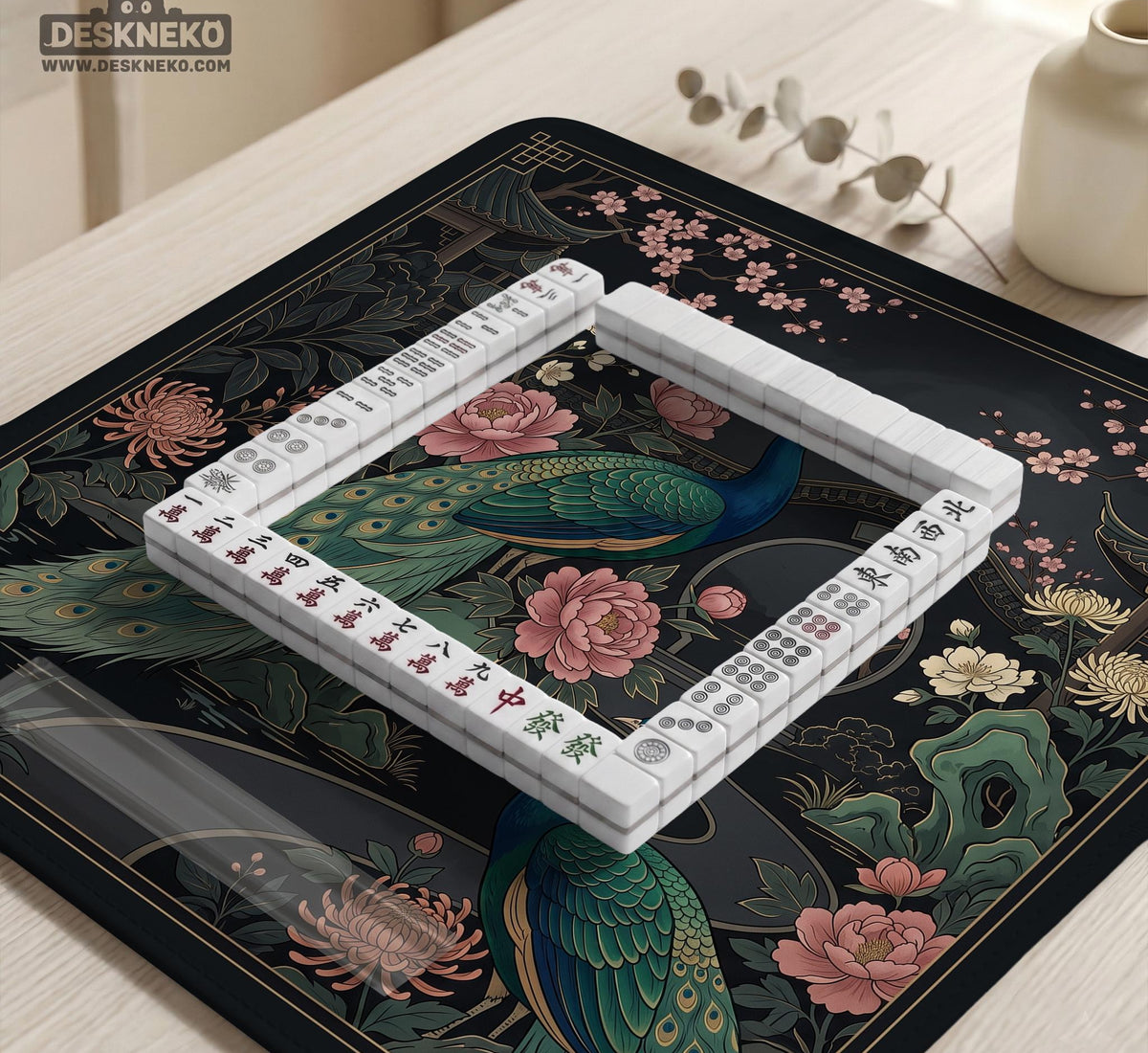 Square black mahjong mat with a gold peacock, blush flowers, and dark botanical artwork on a dark background.