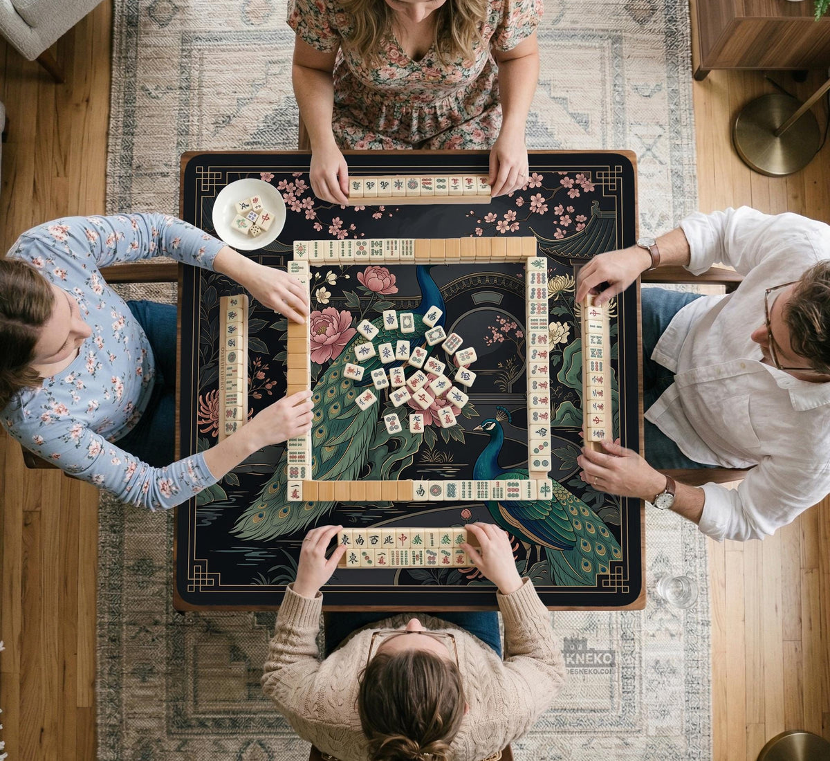 Square black mahjong mat with a gold peacock, blush flowers, and dark botanical artwork on a dark background.