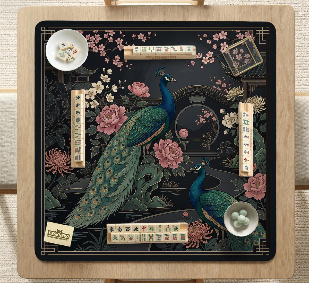 Square black mahjong mat with a gold peacock, blush flowers, and dark botanical artwork on a dark background.