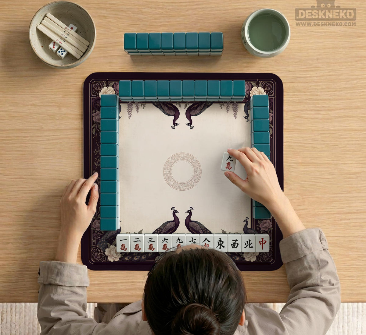 Square mahjong mat with a dark plum border, ivory floral pattern, muted sage leaves, and a decorative peacock garden design.