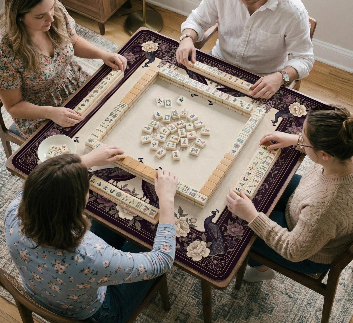 Square mahjong mat with a dark plum border, ivory floral pattern, muted sage leaves, and a decorative peacock garden design.
