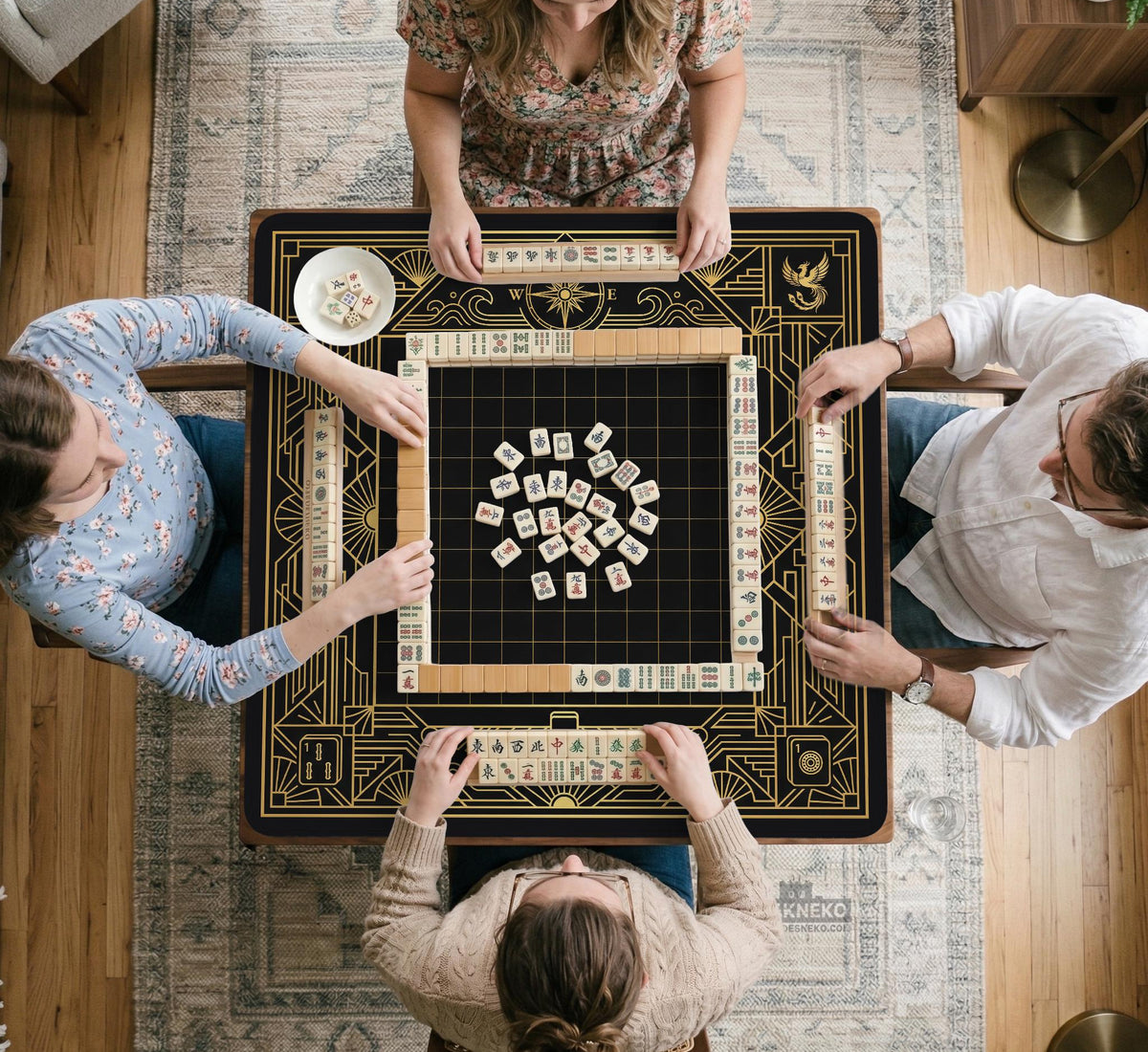 Black and gold square mahjong mat with a scalloped edge, geometric border, thin line details, fan motifs, and dragon and phoenix accents around an open center.