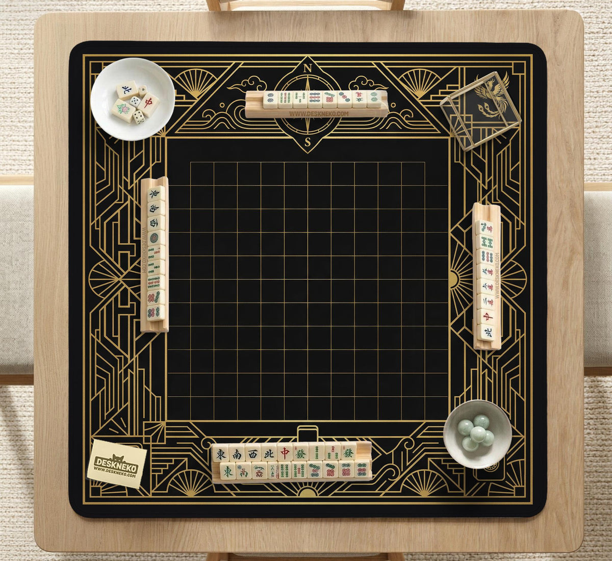 Black and gold square mahjong mat with a scalloped edge, geometric border, thin line details, fan motifs, and dragon and phoenix accents around an open center.