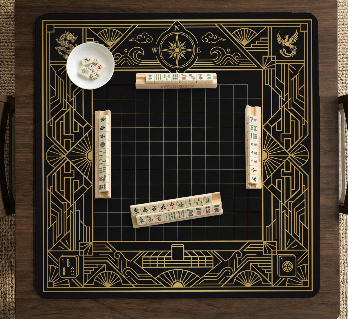 Black and gold square mahjong mat with a scalloped edge, geometric border, thin line details, fan motifs, and dragon and phoenix accents around an open center.