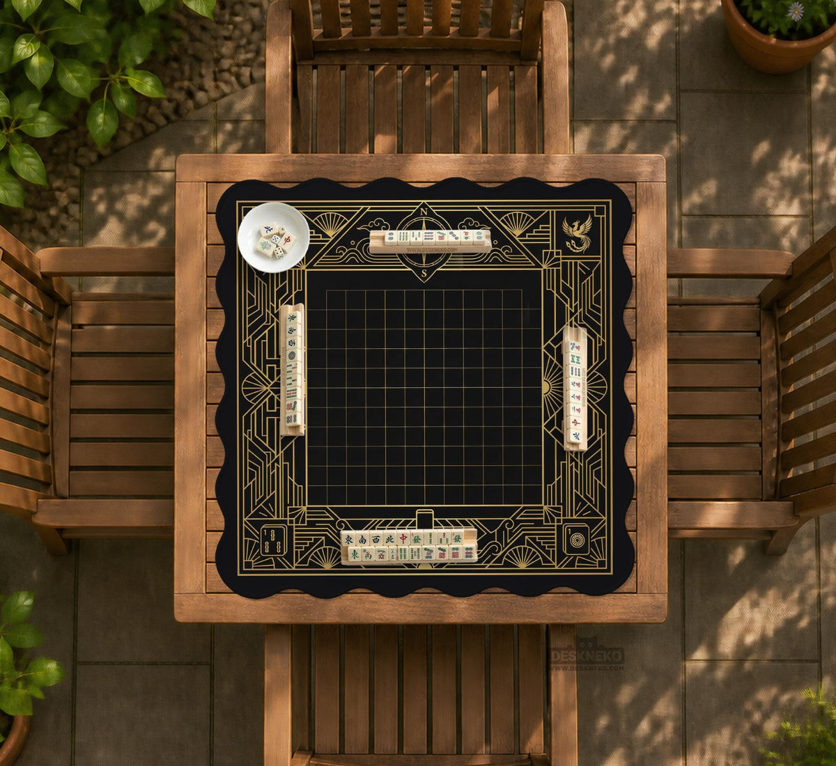 Black and gold square mahjong mat with a scalloped edge, geometric border, thin line details, fan motifs, and dragon and phoenix accents around an open center.