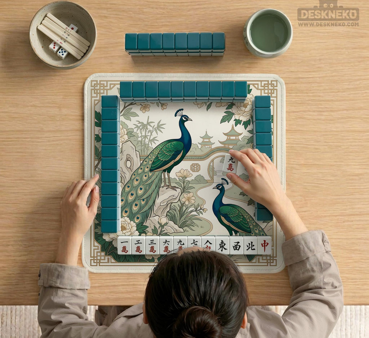 A green mahjong mat with peacock, floral, bamboo, pagoda, and gold border artwork in a scalloped chinoiserie style.