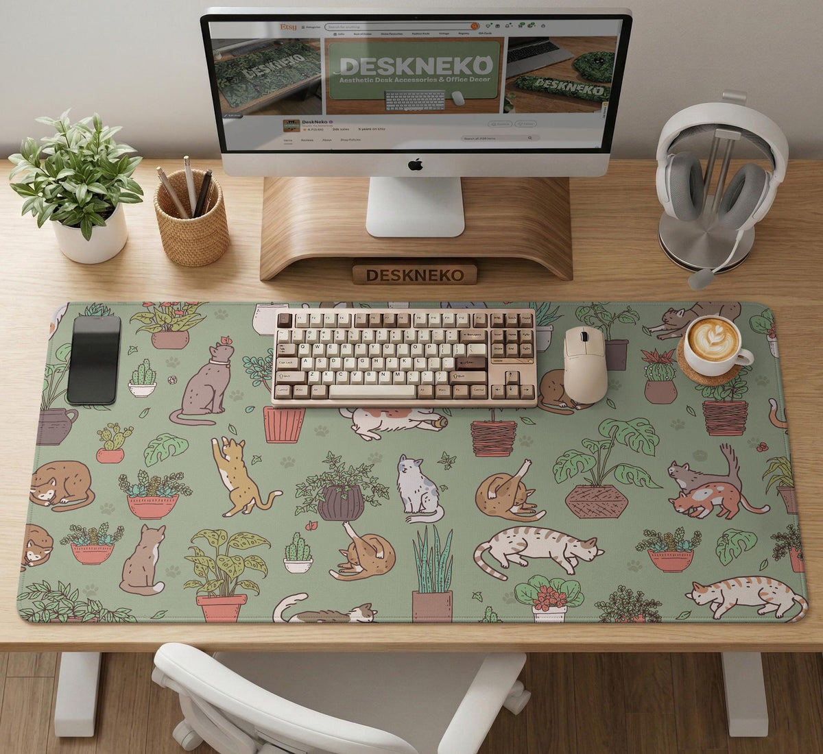A desk mat with a repeating pattern of cats, leafy houseplants, cactus pots, and small plant-shop style details in sage green.