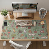 A desk mat with a repeating pattern of cats, leafy houseplants, cactus pots, and small plant-shop style details in sage green.