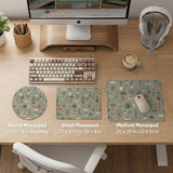 A desk mat with a repeating pattern of cats, leafy houseplants, cactus pots, and small plant-shop style details in sage green.