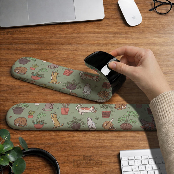 Sage green desk mat with a pattern of lounging cats, leafy plants, cactus pots, and earthy botanical details.