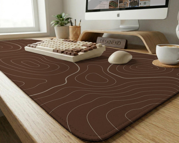 Brown desk mat with a repeating topographic contour line pattern in a neutral earth tone design.