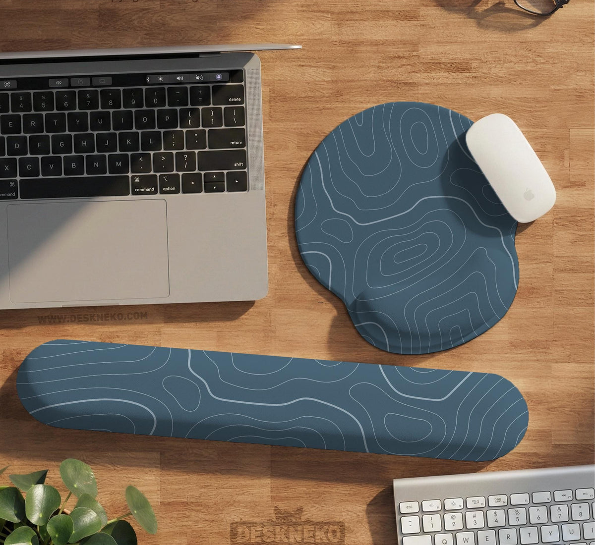 Muted blue desk mat with thin topographic line art pattern shown with matching mousepad and keyboard wrist rest options.
