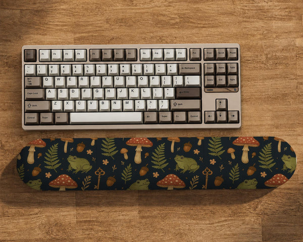 Dark botanical desk mat options with frogs, mushrooms, ferns, and acorns in brown and green tones, plus a matching keyboard wrist rest.