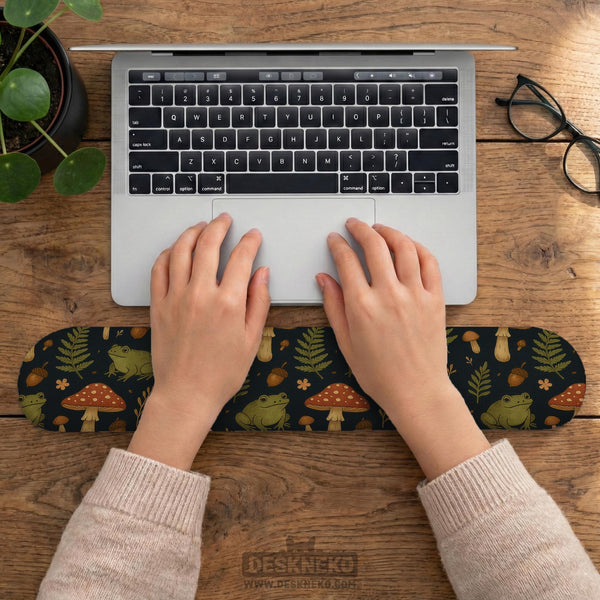Dark botanical desk mat options with frogs, mushrooms, ferns, and acorns in brown and green tones, plus a matching keyboard wrist rest.