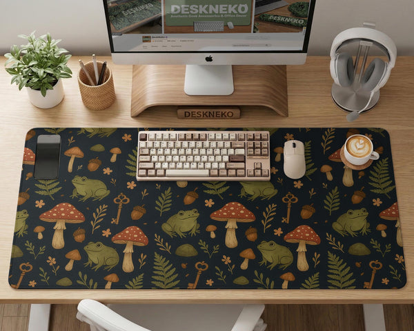 Dark forest-themed desk mat with an all-over pattern of frogs, mushrooms, fern leaves, acorns, tiny flowers, and antique keys.