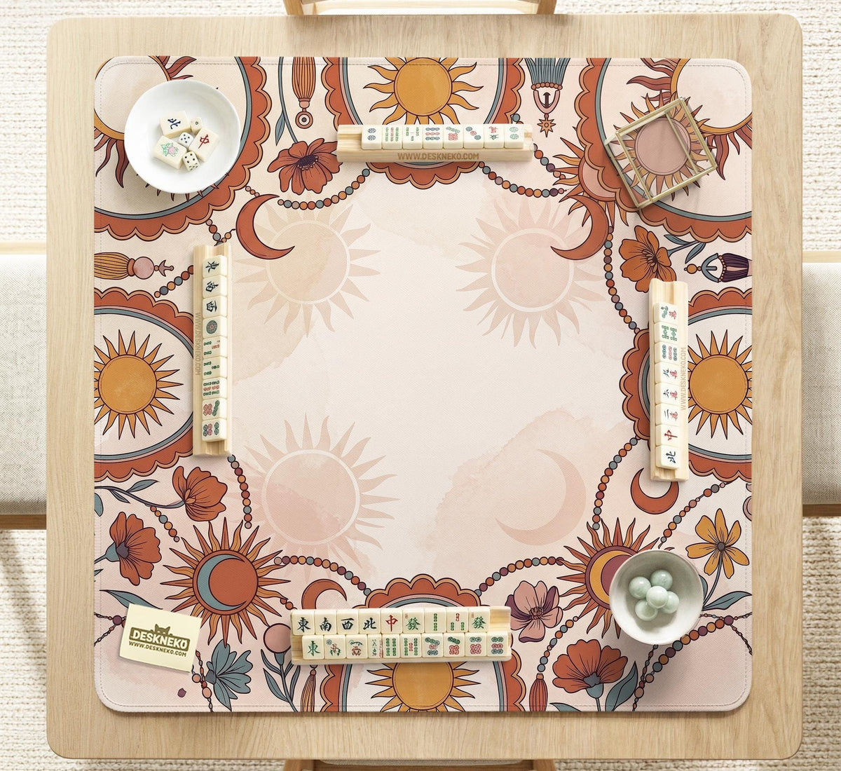 A square mahjong mat with a scalloped edge, sun and moon artwork, terracotta flowers, a soft cream background, and a decorative border around the play area.