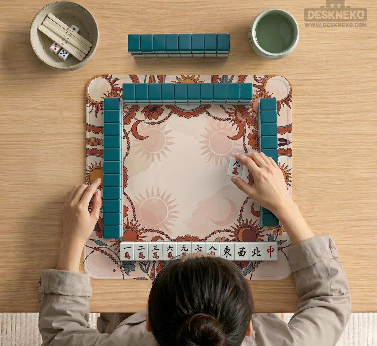 A square mahjong mat with a scalloped edge, sun and moon artwork, terracotta flowers, a soft cream background, and a decorative border around the play area.