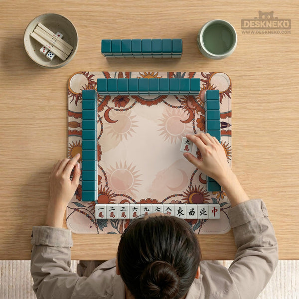 A square mahjong mat with a scalloped edge, sun and moon artwork, terracotta flowers, a soft cream background, and a decorative border around the play area.