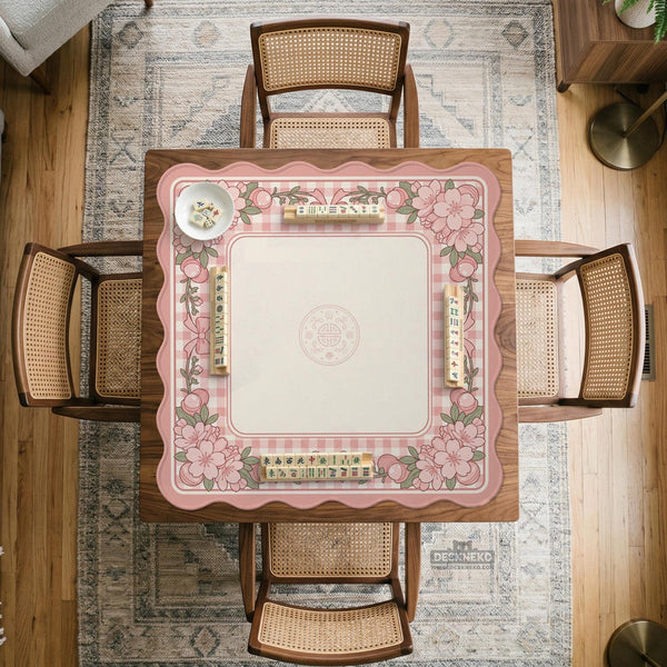 Square pink mahjong mat with a gingham border, floral corner details, and ribbon accents on a light background.