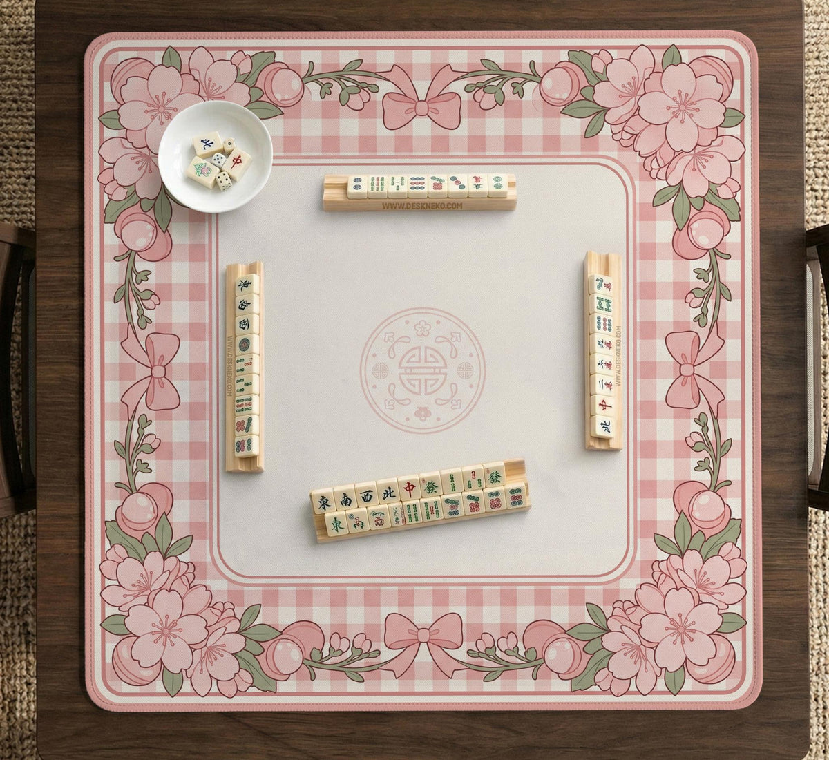 Square pink mahjong mat with a gingham border, floral corner details, and ribbon accents on a light background.