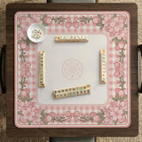 Square pink mahjong mat with a gingham border, floral corner details, and ribbon accents on a light background.