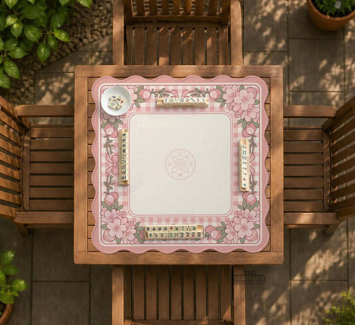 Square pink mahjong mat with a gingham border, floral corner details, and ribbon accents on a light background.