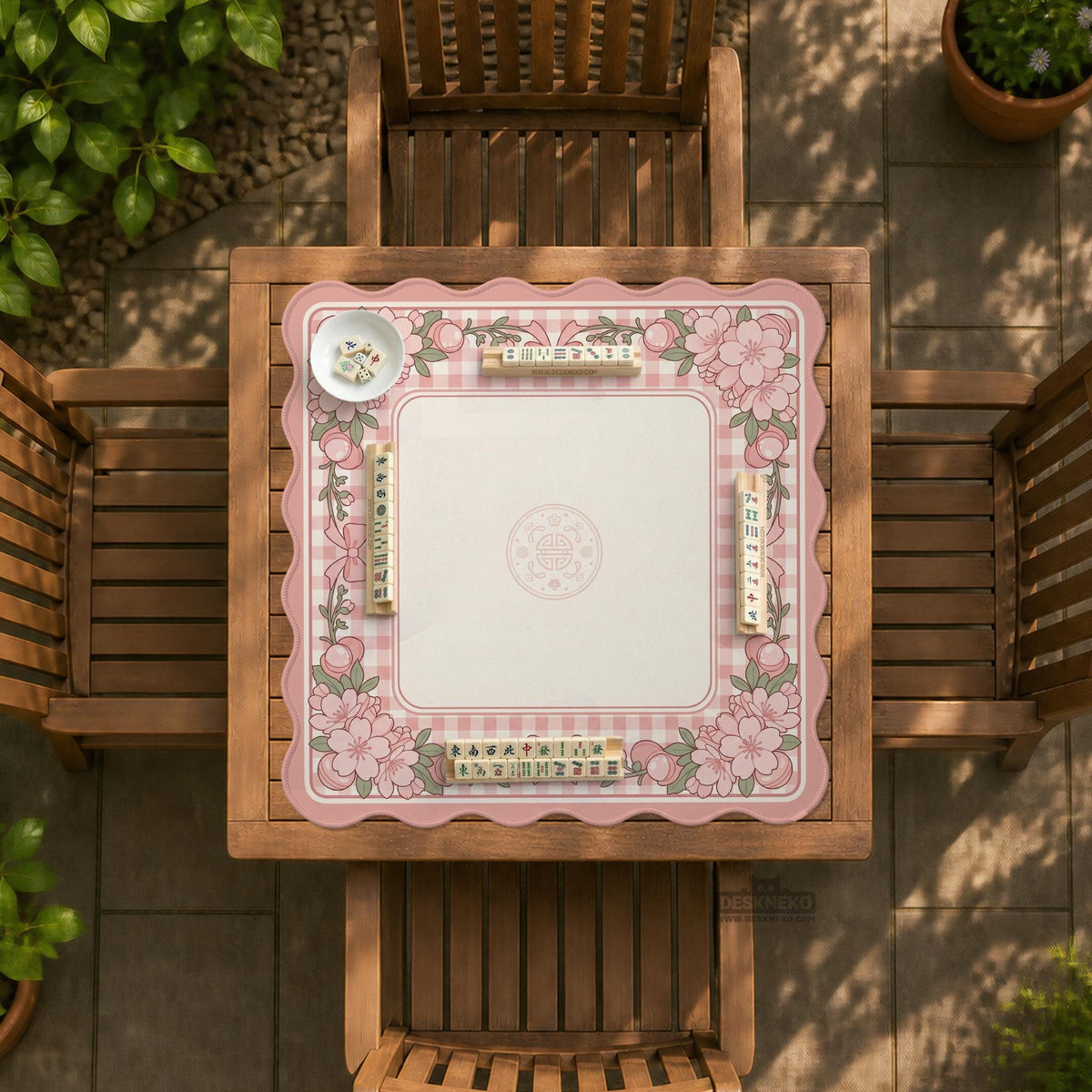 Square pink mahjong mat with a gingham border, floral corner details, and ribbon accents on a light background.