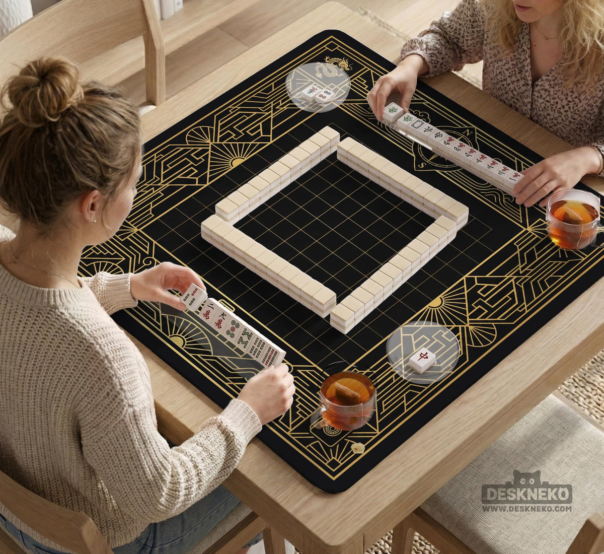 Black and gold square mahjong mat with a scalloped edge, geometric border, thin line details, fan motifs, and dragon and phoenix accents around an open center.
