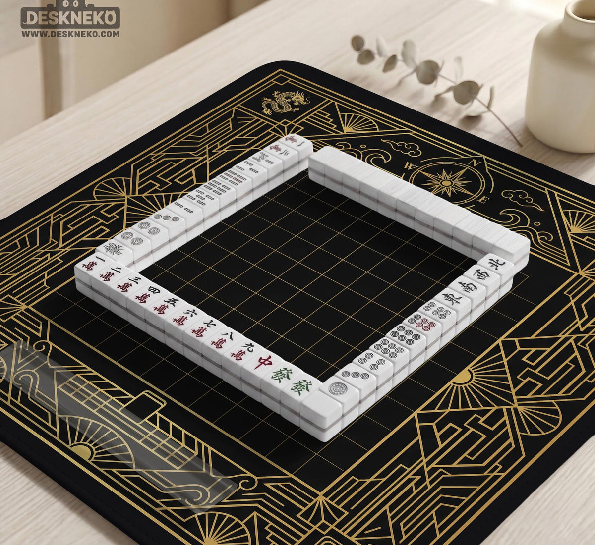 Black and gold square mahjong mat with a scalloped edge, geometric border, thin line details, fan motifs, and dragon and phoenix accents around an open center.