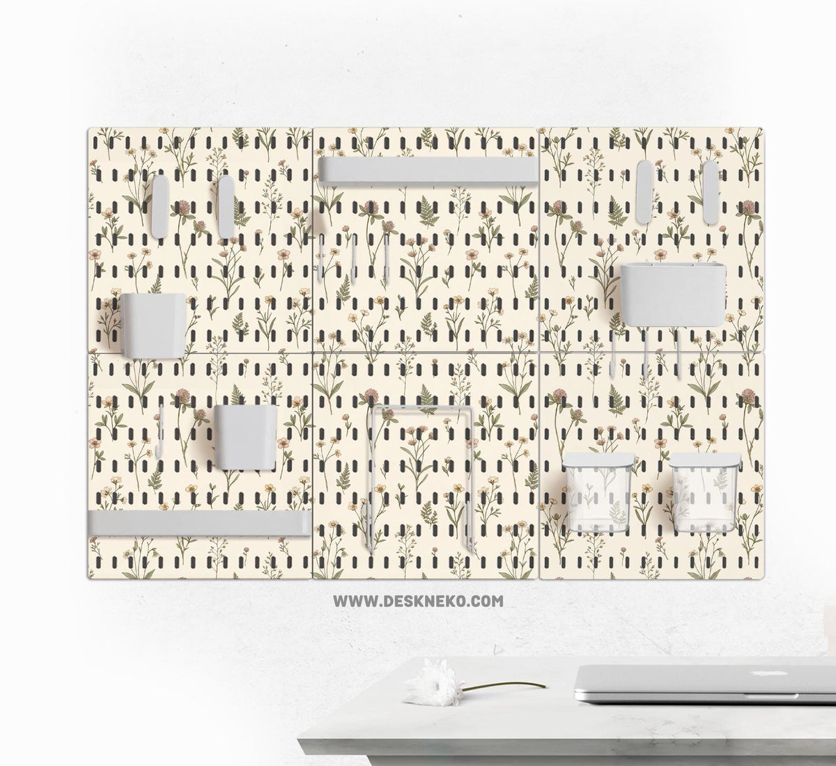 Cream pegboard wall organizer with small floral print, sage green stems, black slot layout, shelves, hooks, clips, and containers.