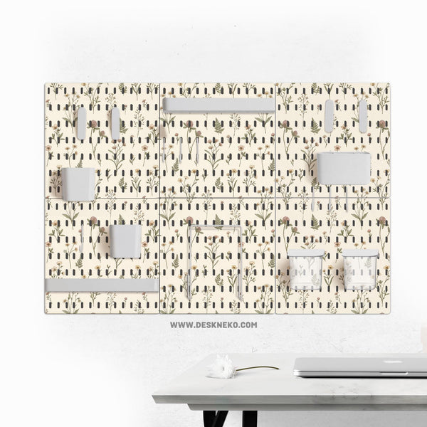 Cream pegboard wall organizer with small floral print, sage green stems, black slot layout, shelves, hooks, clips, and containers.