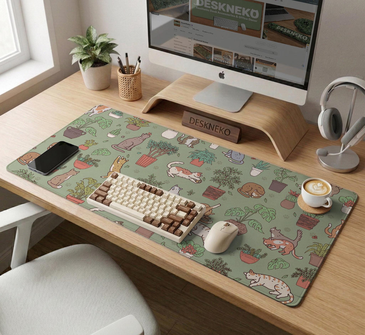A desk mat with a repeating pattern of cats, leafy houseplants, cactus pots, and small plant-shop style details in sage green.