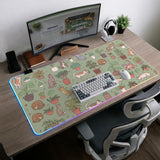 A desk mat with a repeating pattern of cats, leafy houseplants, cactus pots, and small plant-shop style details in sage green.