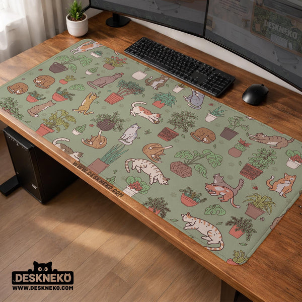 A desk mat with a repeating pattern of cats, leafy houseplants, cactus pots, and small plant-shop style details in sage green.