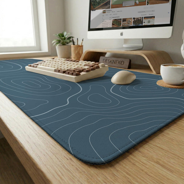 A slate blue desk mat with thin contour line map art on a light background.