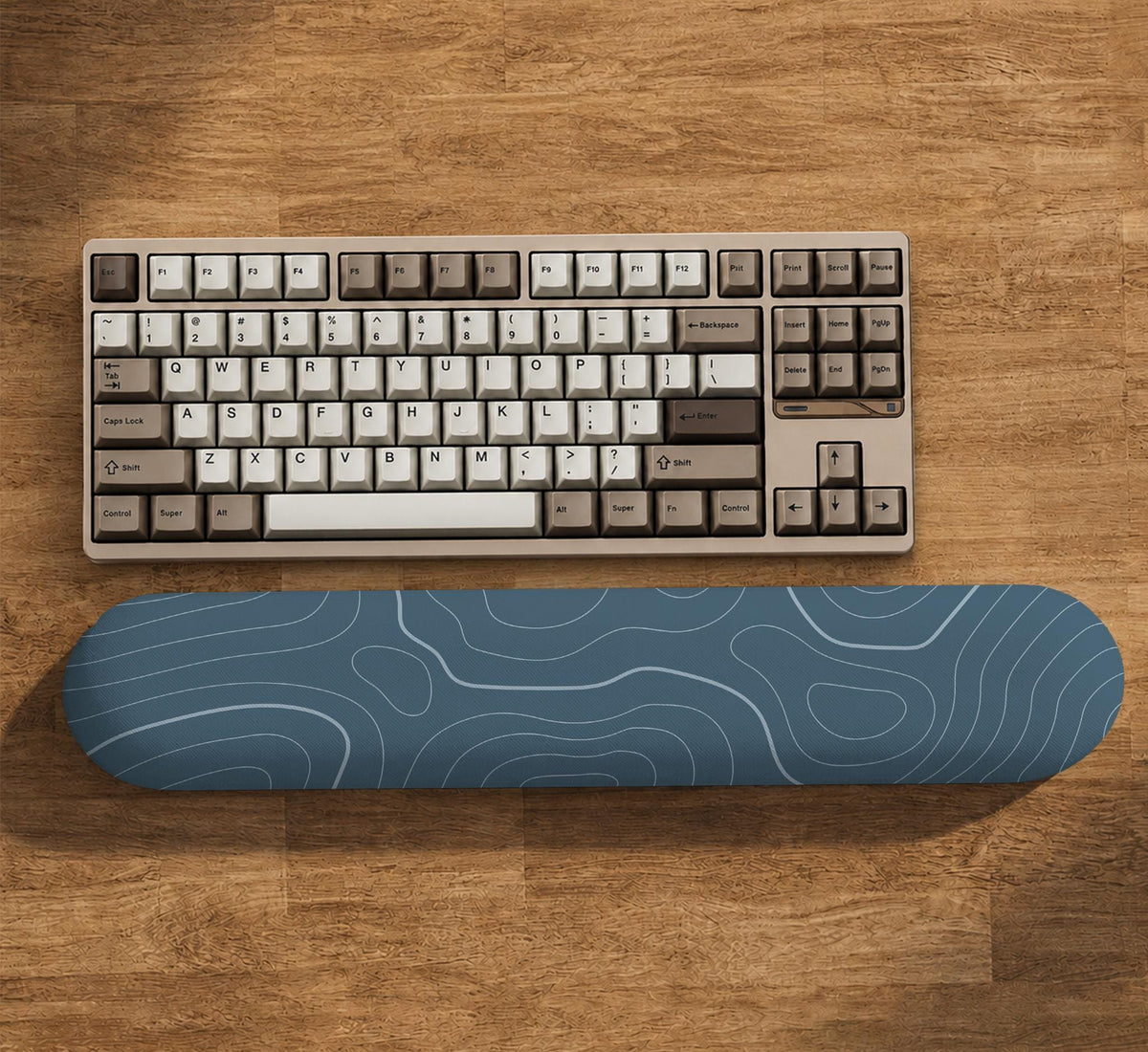 Muted blue desk mat with thin topographic line art pattern shown with matching mousepad and keyboard wrist rest options.