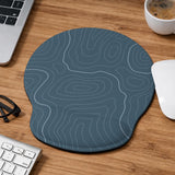 Muted blue desk mat with thin topographic line art pattern shown with matching mousepad and keyboard wrist rest options.