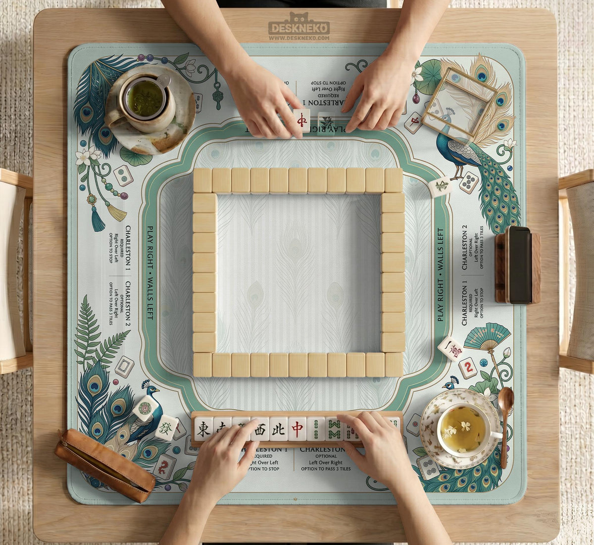 Teal square mahjong mat with peacock feathers, soft floral pattern, tassel details, and printed rule guide text in the center.